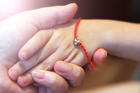 Red thread with a heart of gold on the child's hand so closeの写真素材