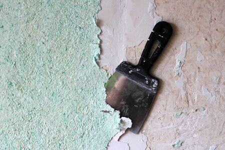 Demolished wallpaper with underlying raw wall and spatula behind it, old plaster , holes and cracks are tampedの写真素材
