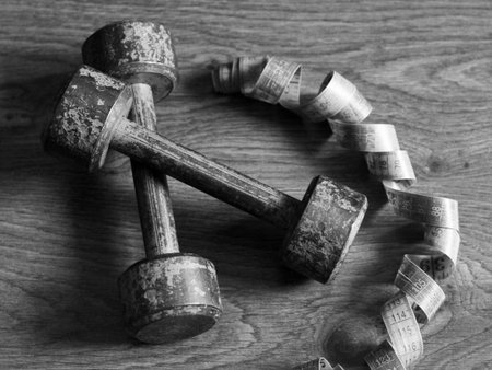 Old iron collapsible dumbbells and a meter tape on the wooden floor, top view