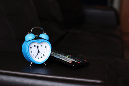 Blue alarm clock in the shape of a heart and remote TV, leather sofa