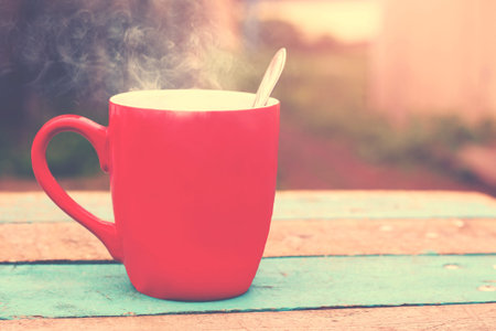 Red mug with hot coffee on a wooden table, natural background, drink