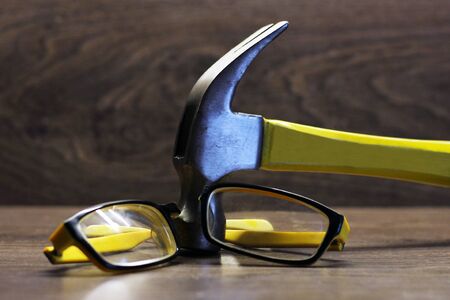 Broken yellow glasses and a hammer on wooden backgroundの写真素材