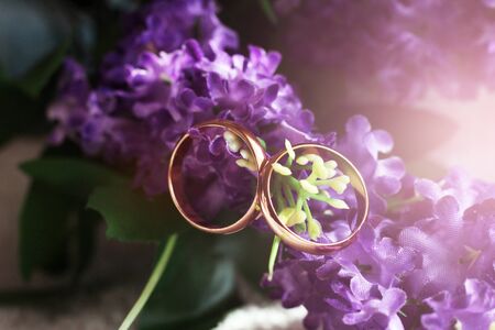 wedding details: two golden wedding rings on a purple flower petal of a wedding bouquetの写真素材