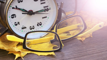Broken yellow glasses, golden clock and autumn leaves, wooden background