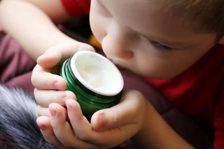 Baby boy little hands holding white cream bottle, a portrait so close, beauty gelの写真素材