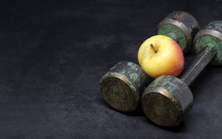 Old iron dumbbells and an apple, sports and diet. Dark background.の写真素材