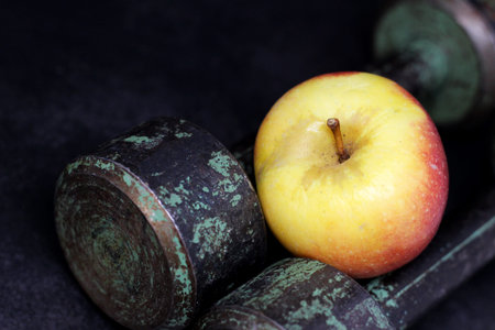 Old iron dumbbells and an apple, sports and diet. Dark background.