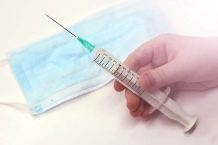 Children's hand holding a syringe, a mask, medicine