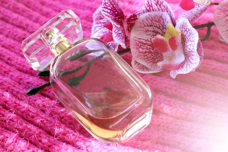 Perfume bottle with orchid flower on pink background, close up