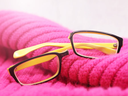 Eyeglasses on pink knitted background. Selective focus.