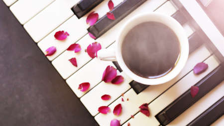 A cup of coffee on the piano and pink rose petalsの写真素材