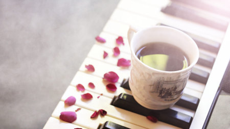 A cup of coffee on the piano and pink rose petals