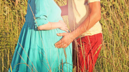 A man embraces a pregnant woman, a man's hands on a woman's stomach, summerの写真素材