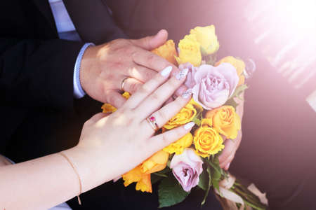 Hands of the bride and groom on the background of a bouquet of flowers.の写真素材