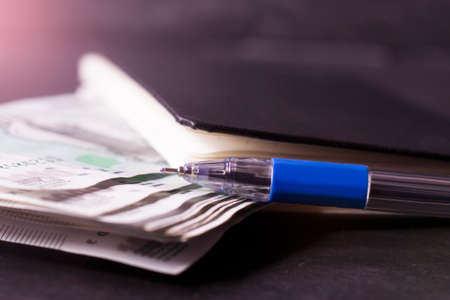 Close-up of a blue pen on top of a notebook with moneyの写真素材