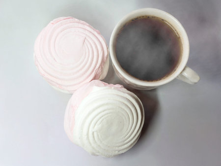 Two white and pink marshmallows and a cup of coffee on a gray backgroundの写真素材