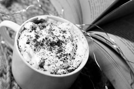 Cup of hot chocolate with whipped cream and book. Black and white photo.の写真素材