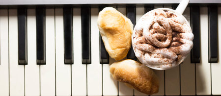 Cup of coffee with marshmallow and croissants on piano keyboard, banner