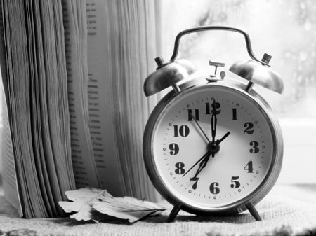 Retro alarm clock and book on a background of glass with raindrops