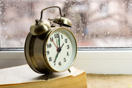 Retro alarm clock and book on a background of glass with raindrops