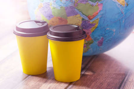 Two yellow cups of coffee and a globe on a wooden table, a world drinkの写真素材