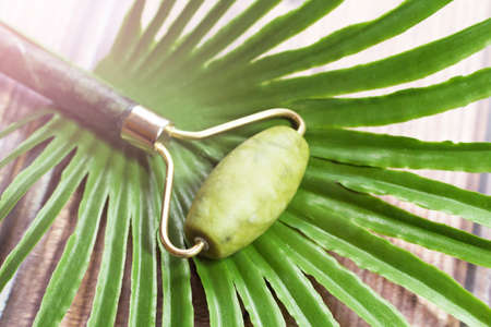 Green jade face roller and palm leaf on a wooden background.の写真素材