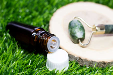 Jade face roller and jar of essential oil on green grass.の写真素材