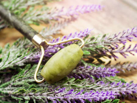 Jade facial massage roller and lavender flowers on wooden background.の写真素材
