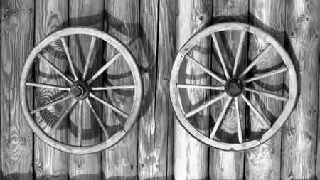 Old wooden wagon wheels on a wooden background. Black and white.の写真素材