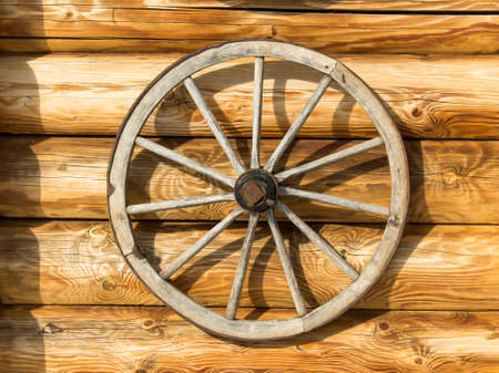 Old wooden wheel on the background of the wall of a log houseの写真素材