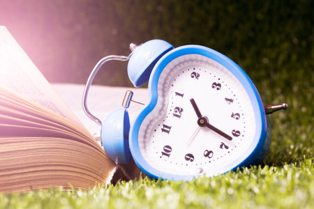 Alarm clock and book on green grass. Time management concept.