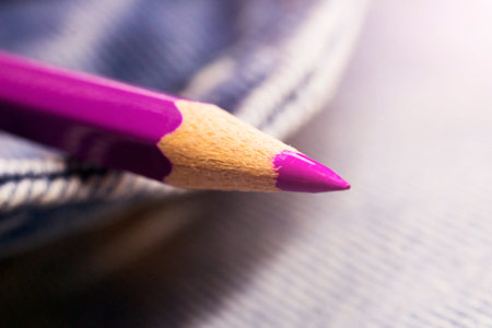 Close up of a pink pencil lying on a blue jeans background.