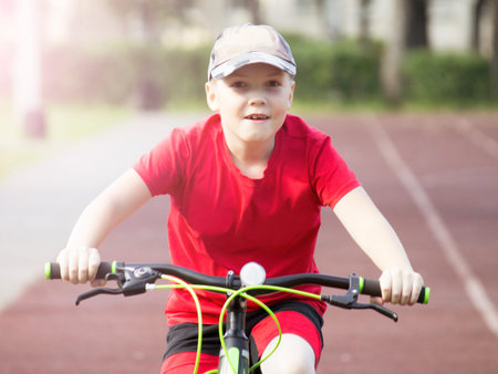 A boy on a bicycle in a red T-shirt rides around the stadium, cyclingの写真素材