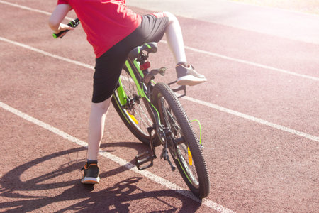 A boy on a bicycle in a red T-shirt rides around the stadium, cycling