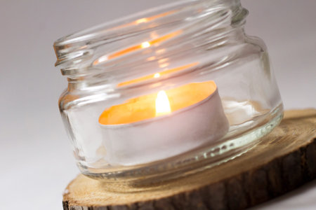 Candle in a glass jar on a wooden stump on a white backgroundの写真素材