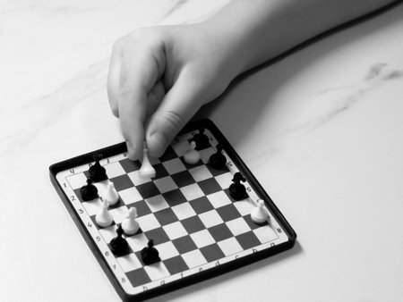 Black and white photo of hand playing chess with black and white chess piecesの写真素材