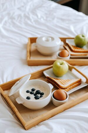 Breakfast in the hotel. Porridge, boiled egg, toast, coffee, porridge with berries on a trayの写真素材