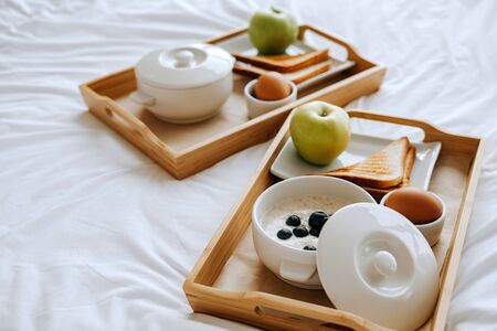 Breakfast in the hotel. Porridge, boiled egg, toast, coffee, porridge with berries on a trayの写真素材