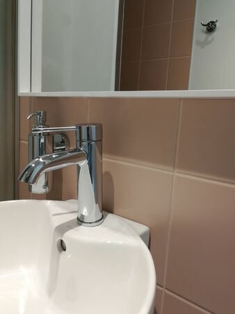 Hotel bathroom interior with round white sink and glossy metal details. Metal bathroom tap, soap dispenser and mirror in front of terra cotta tiles.の写真素材