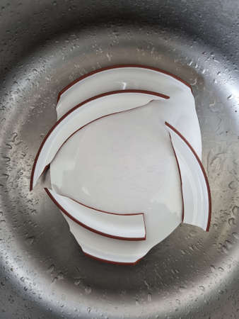 Ceramic plate broke apart. Failure in the kitchen during meal preparation. Dinner plate cracked into pieces. Plate shreds in the sink.の写真素材