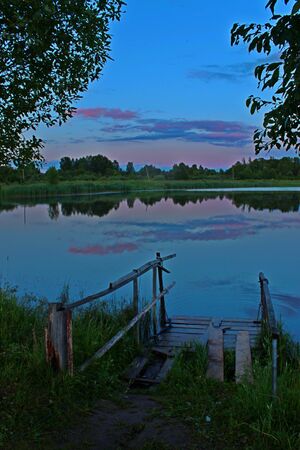 Photo of summer sunset on the shore of the pond near the bridgeの写真素材