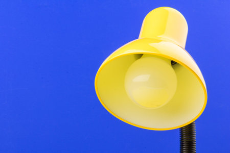 Yellow desk lamp isolated on blue background. The concept of day and nightの写真素材