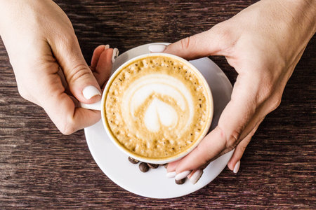 Fresh roasted coffee beans in a white Cup. Hands with a Cup of coffee on the background of a brown...