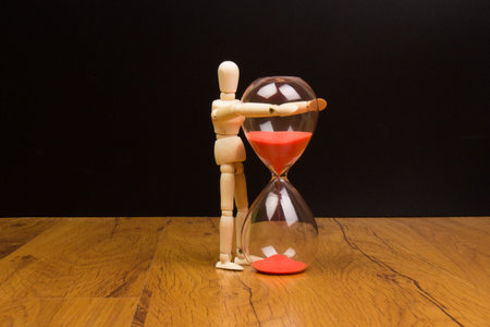 The wooden mannequin next towards the hourglass. keeping time