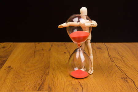 The wooden mannequin next towards the hourglass. keeping timeの写真素材