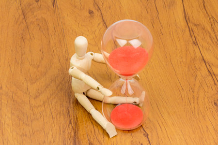 The wooden mannequin next towards the hourglass. keeping time