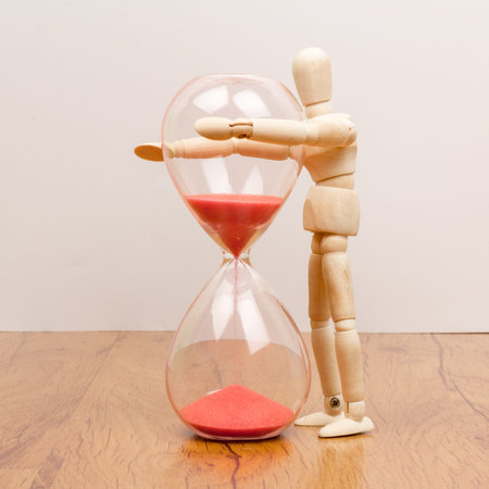 The wooden mannequin next towards the hourglass. keeping time
