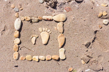 Sand texture. Sandy beach with sea stones for background.Touching picture of sea pebbles on sandy beach. Image of a child's and adult's foot made of stones.の写真素材