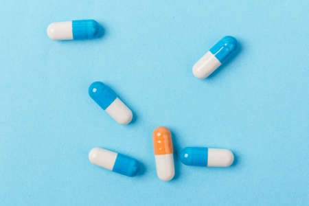 Blue and white capsules and orange whith white capsule pill on blue background. Global healthcare concept. Antibiotics drug resistance. Pharmaceutical industry.の写真素材