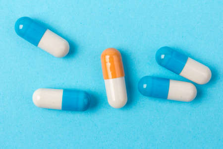 Blue and white capsules and orange whith white capsule pill on blue background. Copy space. Global healthcare concept. Antibiotics drug resistance. Antimicrobial capsule pills. Pharmaceutical industry.の写真素材